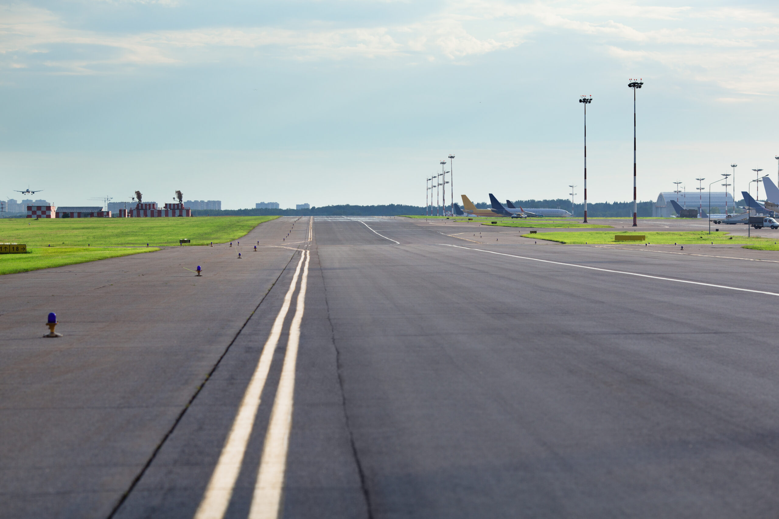 Empty airport asphalt runway with yellow marking, airplanes in the background 